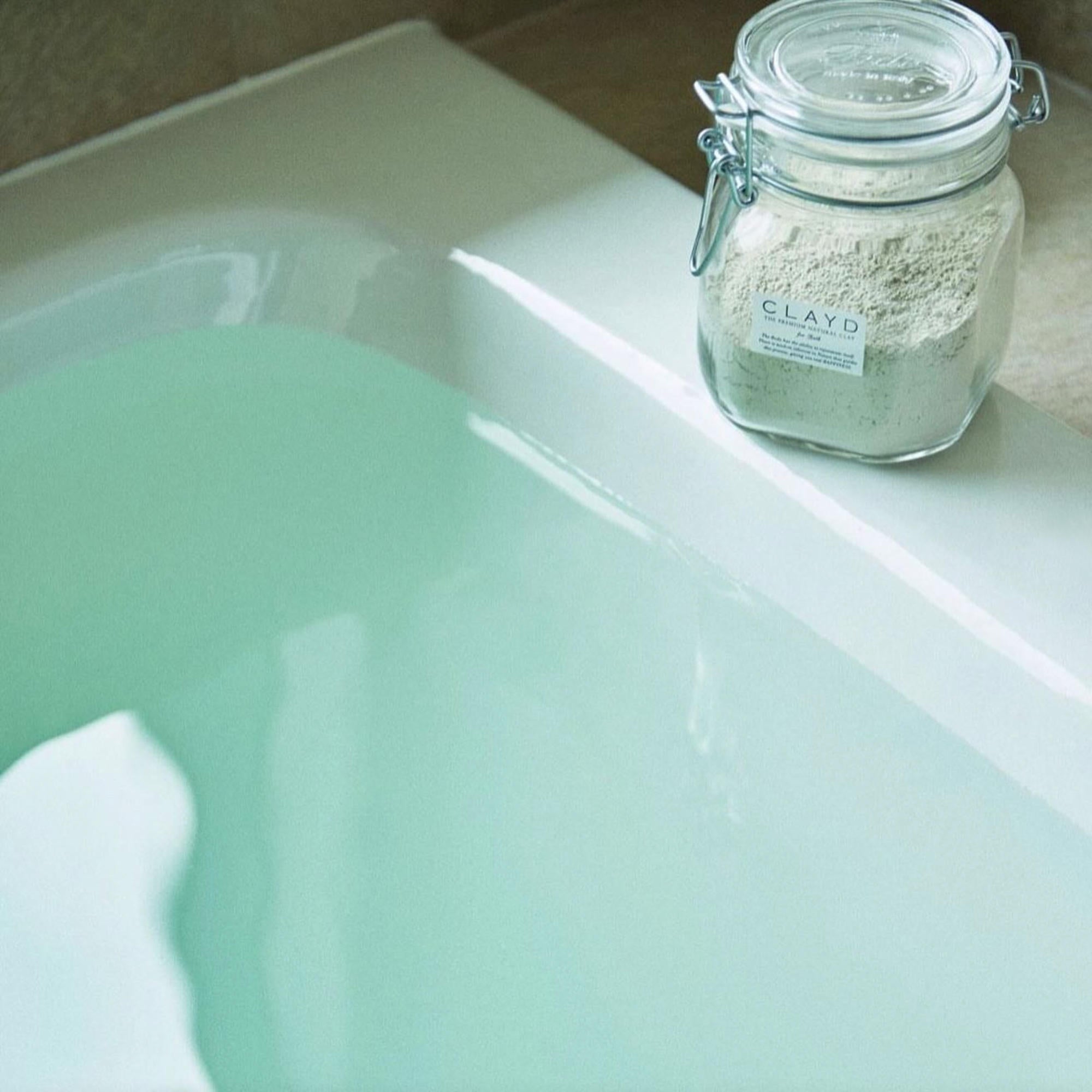 Jar of clay powder on a bathtub with green water